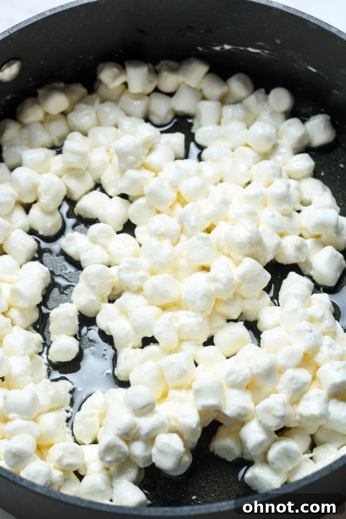 Mini marshmallows melting into a smooth, gooey mixture with butter in a pan