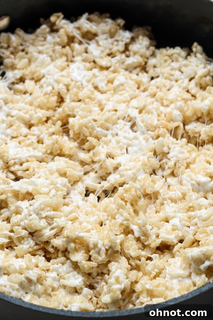 Gluten-free rice cereal being thoroughly stirred into the melted marshmallow and vanilla mixture in a pot