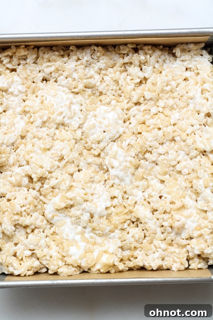 Rice krispies treat mixture gently pressed and flattened into a parchment-lined square pan