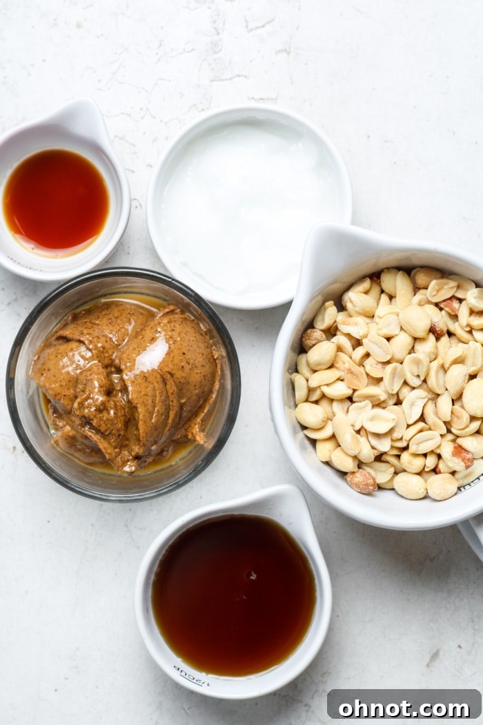 A collection of ingredients laid out, including peanuts, maple syrup, peanut butter, coconut oil, and vanilla extract.