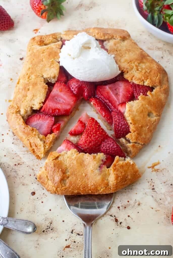 A slice of warm gluten-free strawberry galette topped with a scoop of creamy vanilla ice cream, ready to be enjoyed as a dessert.