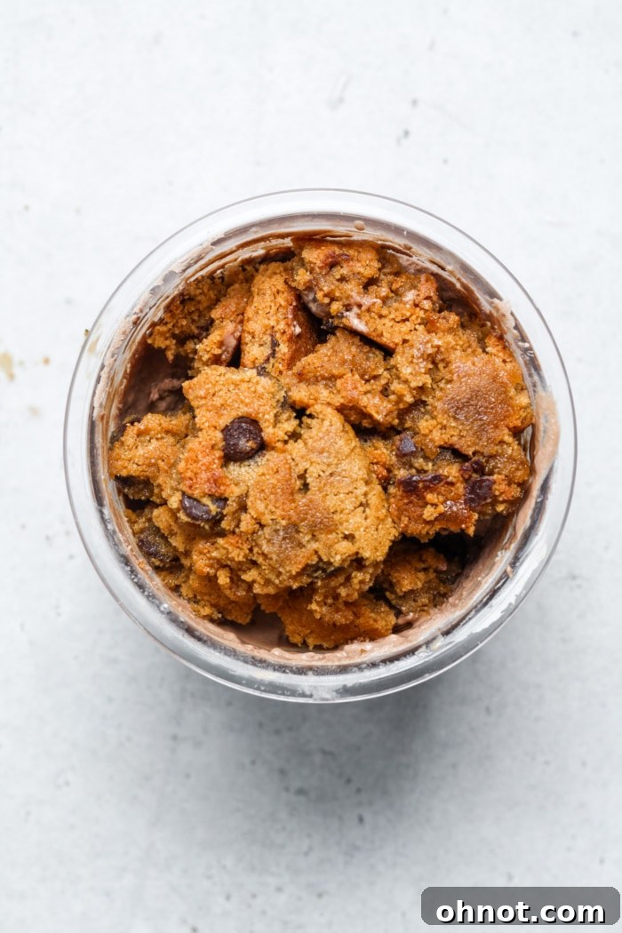 Close-up of creamy chocolate ice cream with a crumbled cookie on top, ready to be enjoyed.