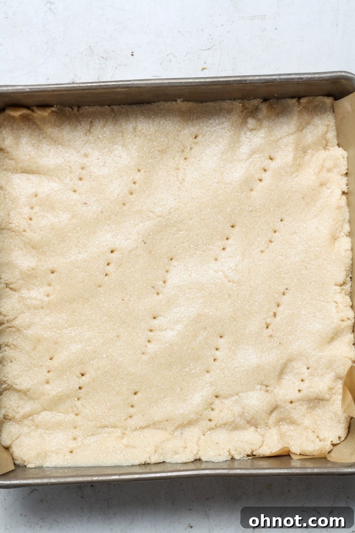 Shortbread dough pressed into a square baking pan, with fork marks visible.