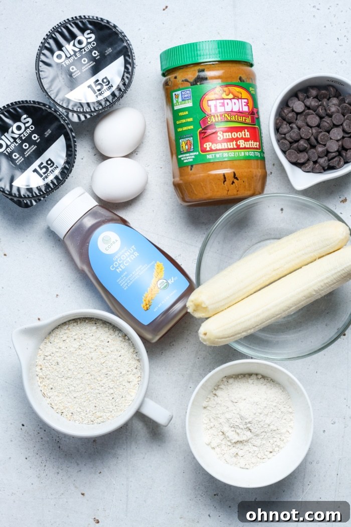 A flat lay of fresh, ripe bananas, eggs, Greek yogurt, peanut butter, oats, oat flour, and chocolate chips – all the ingredients needed for making delicious banana bread bars.