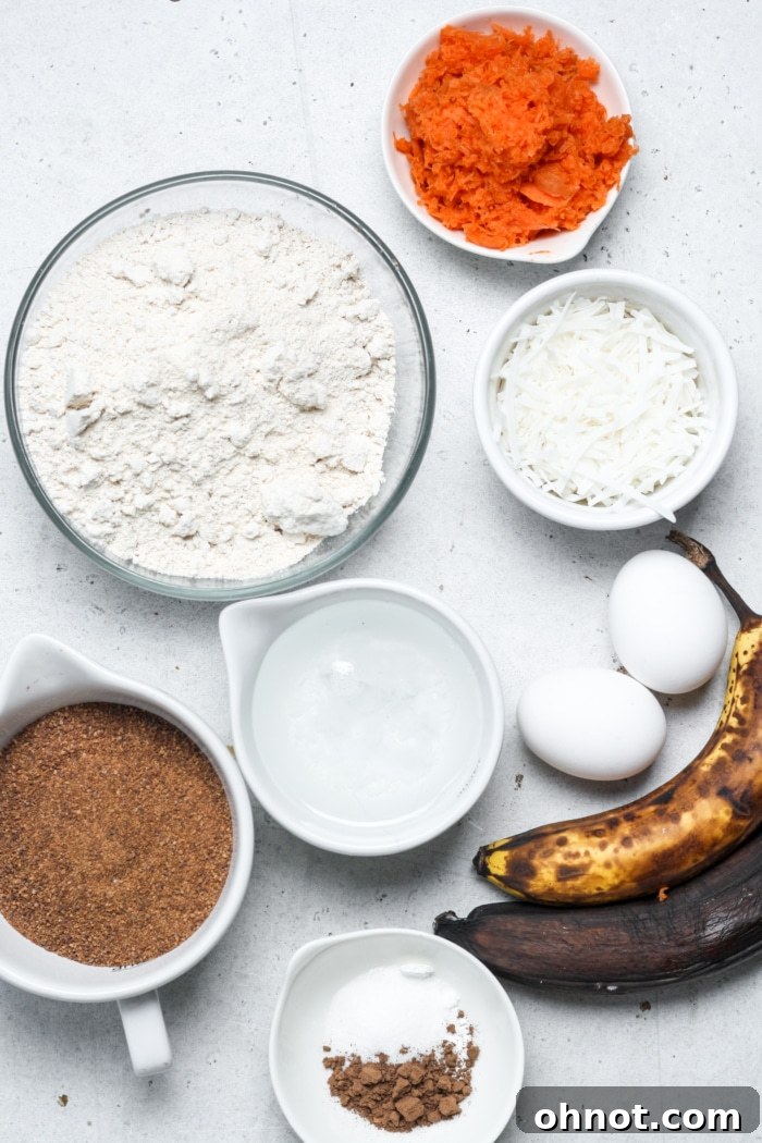 Collection of fresh ingredients for carrot cake banana bread, including ripe bananas, grated carrots, eggs, coconut oil, spices, and oat flour, neatly arranged on a kitchen counter.