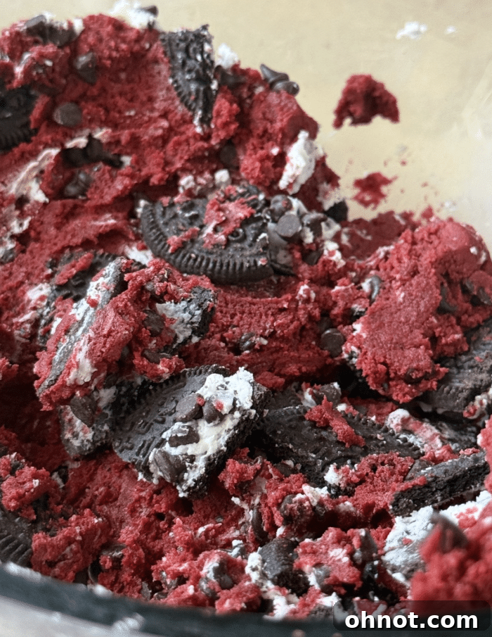 Close-up of red cookie dough with Oreo chunks and chocolate chips folded in.