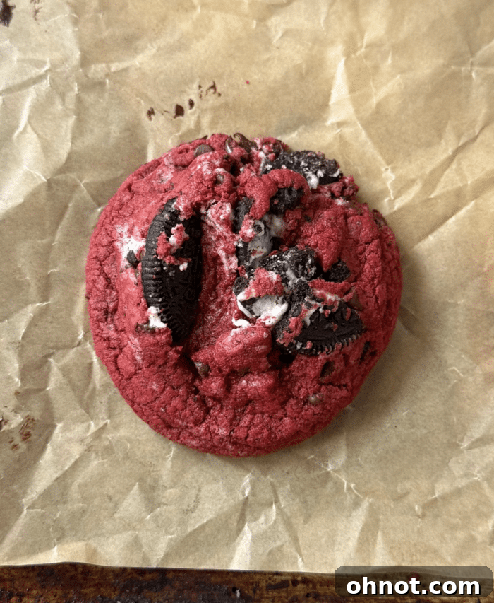 A close-up shot of a chunky, bright red velvet cookie, highlighting its texture and ingredients.