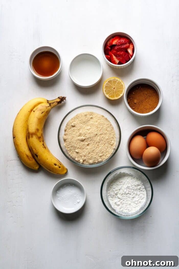 A selection of fresh ingredients including bananas, eggs, strawberries, and flours, laid out for making strawberry banana bread.