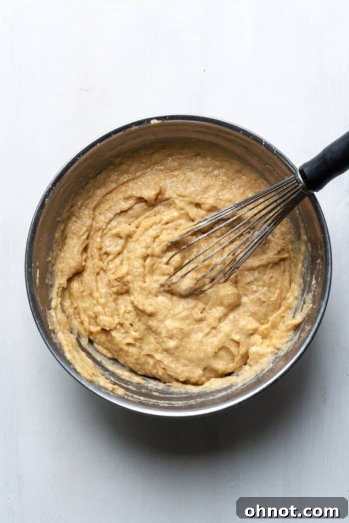 A silver mixing bowl containing a light-colored batter for Paleo strawberry banana bread.
