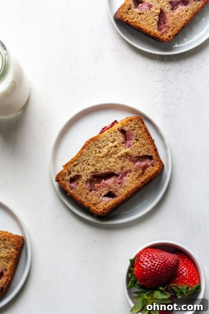 A slice of Paleo strawberry banana bread on a white plate, showcasing its moist texture and fruit pieces.