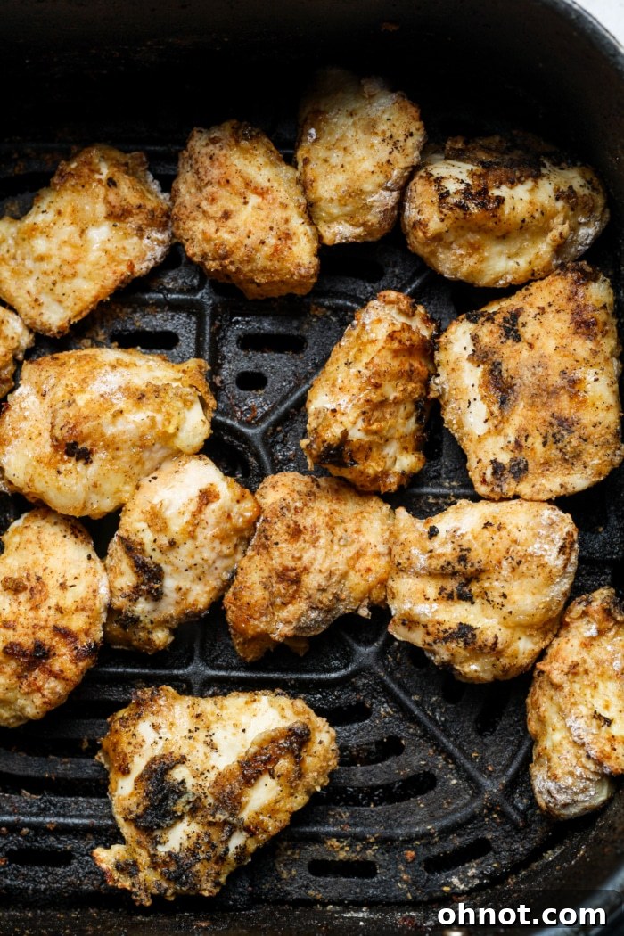 Freshly cooked, crispy chicken pieces being removed from the air fryer basket.