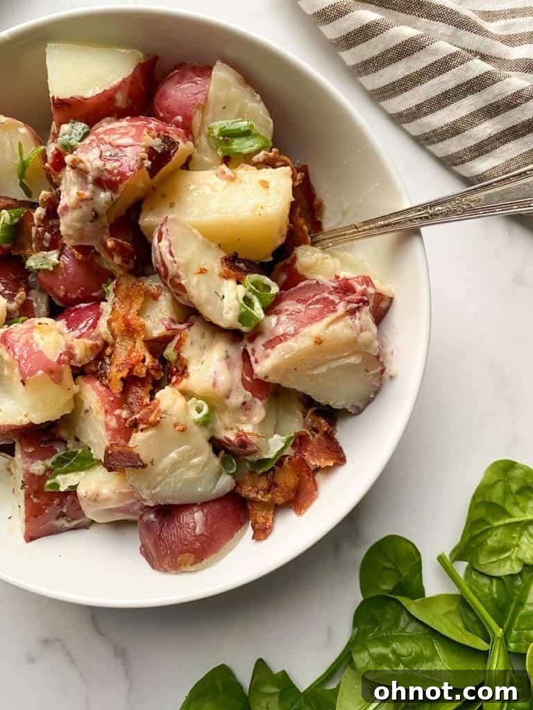 Close-up of the finished Whole30 potato salad in a white bowl, generously topped with crumbled bacon and chopped green onions, highlighting its vibrant texture and inviting appearance.