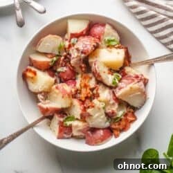A white bowl filled with creamy Dairy Free Whole30 Bacon Ranch Potato Salad, garnished with fresh herbs and crispy bacon.