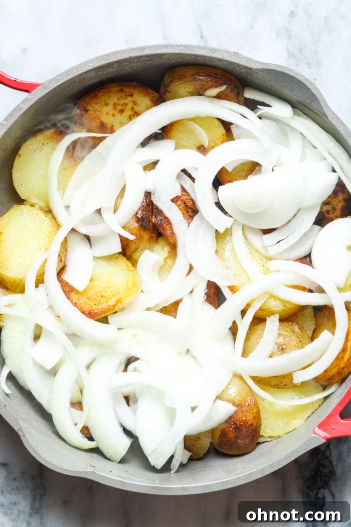 Sliced onions added to cooking potatoes in skillet