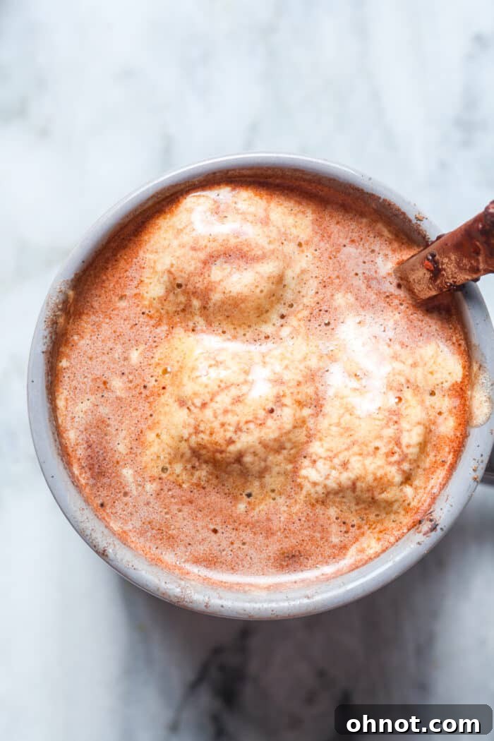 A mug of bone broth hot chocolate, garnished with a sprinkle of cinnamon, sitting on a rustic wooden surface next to a stack of books and a cozy blanket.