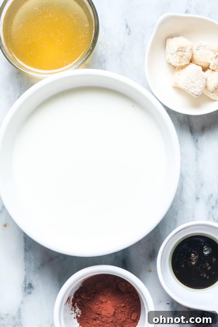 All the core ingredients for making bone broth hot chocolate laid out on a clean white surface: unflavored bone broth carton, a glass of milk, a bowl of cocoa powder, a jar of honey, and a small dish of cinnamon.