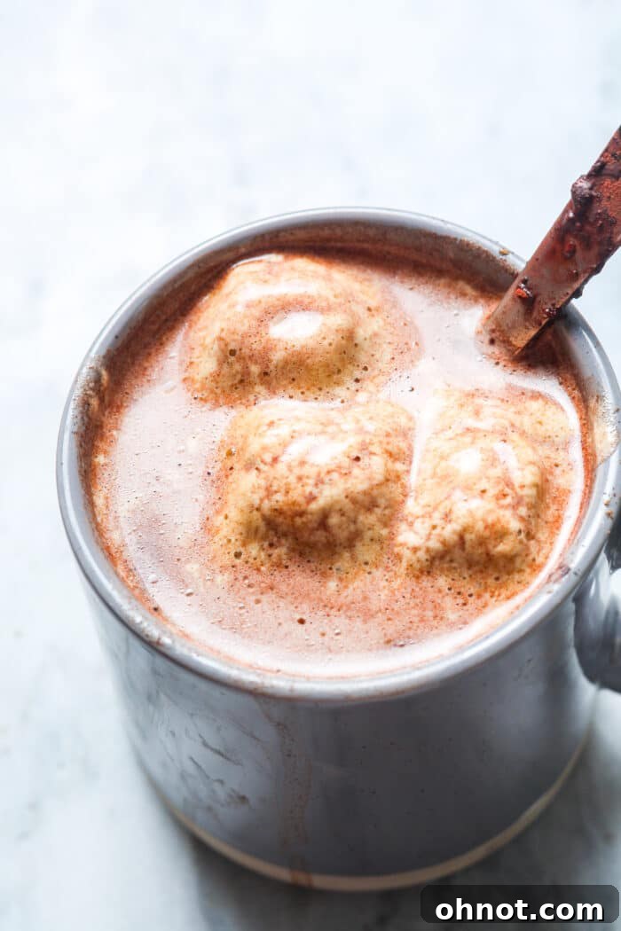 A steaming mug of bone broth hot chocolate, topped with a frothy layer, presented against a blurred background, emphasizing its warmth and inviting appearance.