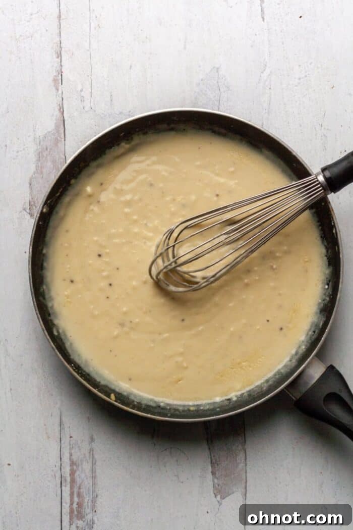 Thickening dairy-free cream sauce for Whole30 Scalloped Potatoes in a skillet, gently simmering on the stovetop.