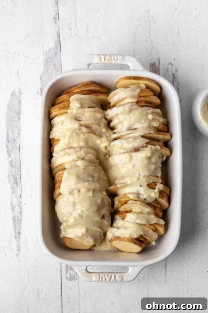 Arranging thin potato slices in a casserole dish and pouring the rich Whole30 sauce over them, ready for baking.