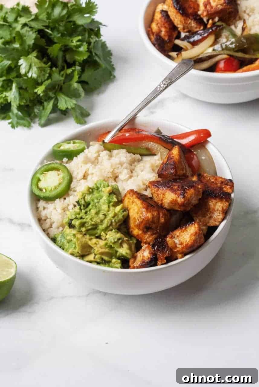 Overhead view of a vibrant chicken fajita bowl being assembled, featuring cooked chicken, colorful vegetables, and cauliflower rice.