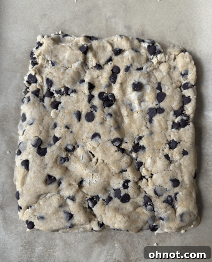 A square of raw cookie dough on parchment paper, ready for chilling and slicing.