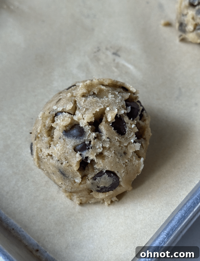 Portioned chocolate chip cookie dough ball on parchment paper, ready to bake.