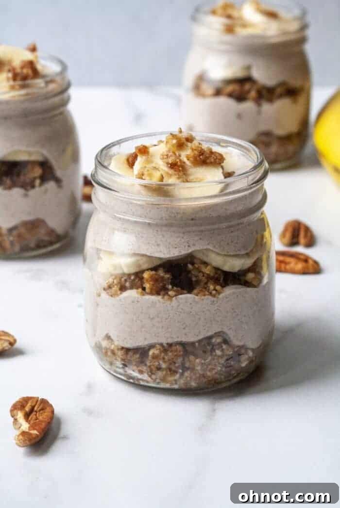 Delicious layers of no-bake banana cream pie in a jar, featuring a nutty crust, creamy banana filling, and fresh banana slices, topped with pecans.