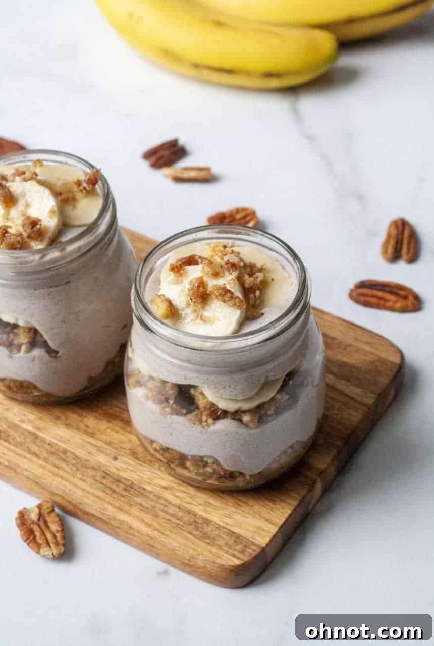 A top-down view of three individual banana cream pie jars, showcasing the distinct layers of crust, cream, and fresh banana slices, garnished with pecans.
