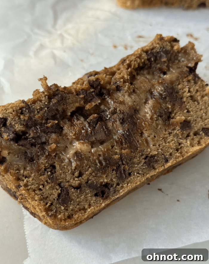 A perfectly sliced piece of Cookie Dough Peanut Butter Bread, revealing a moist interior, melted chocolate chips, and distinct cookie dough layers.