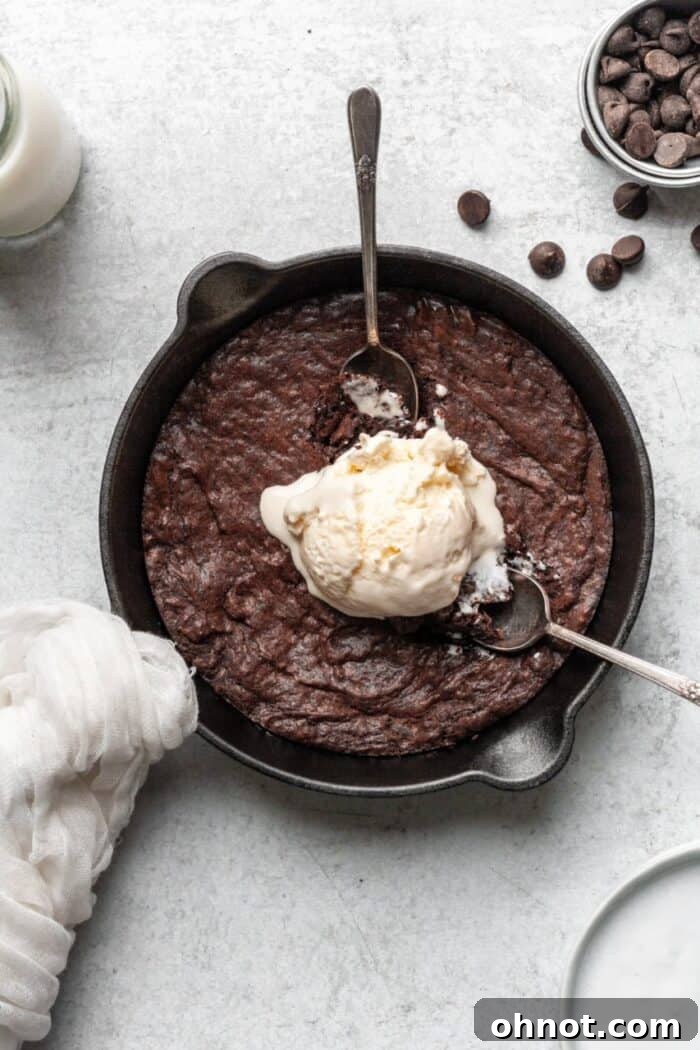 Warm Paleo brownie in a cast iron skillet topped with a scoop of vanilla ice cream, ready to be enjoyed.