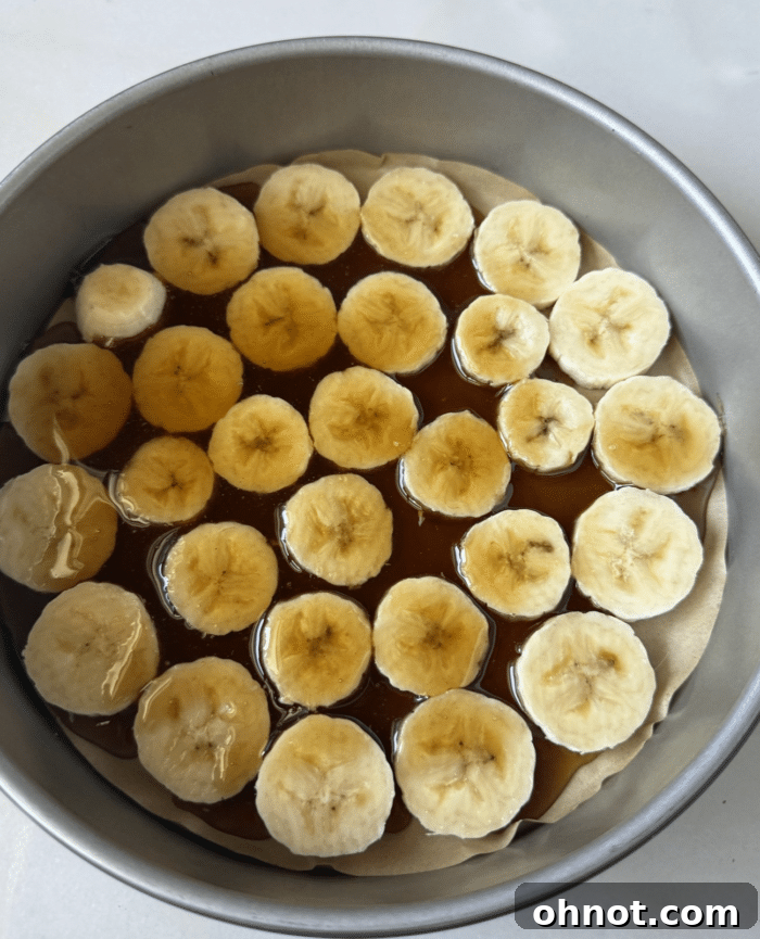 Banana slices arranged in a pan with simmering caramel.