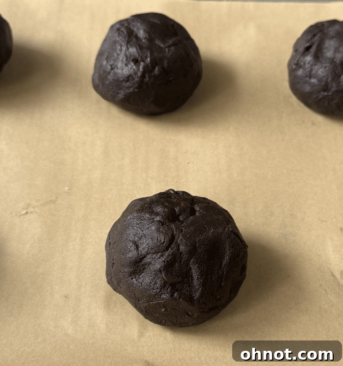 A perfectly formed chocolate cookie dough ball with a visible chocolate square sealed inside, ready for the oven.