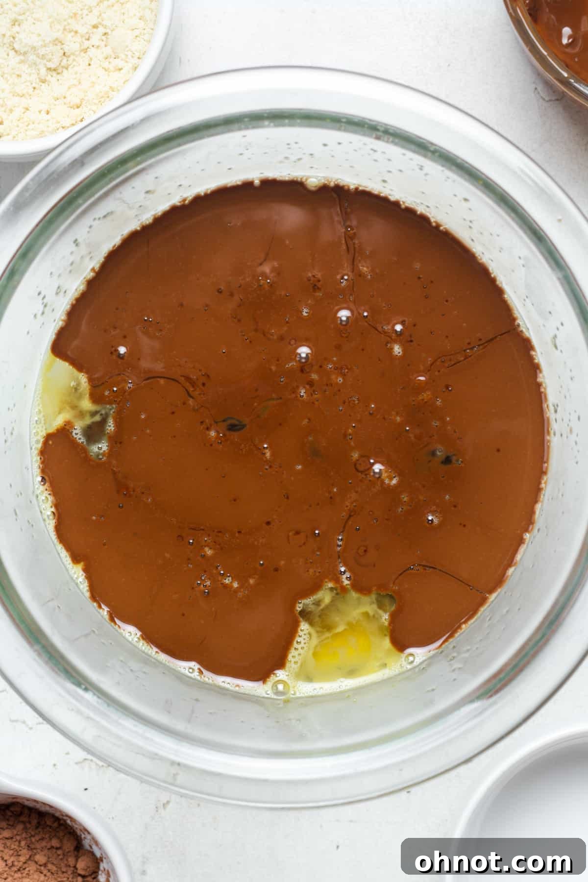 Melted chocolate mixture being slowly poured into the whisked eggs and sugar.