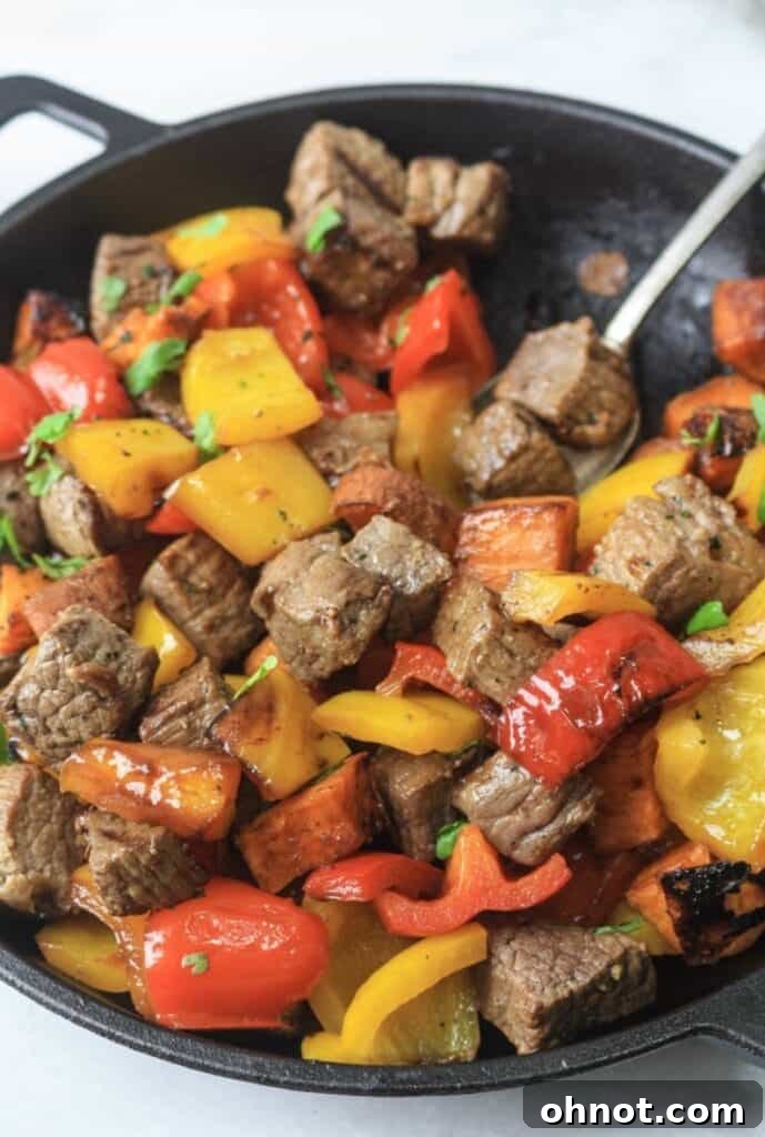 Close-up shot of Whole30 steak bites, sweet potatoes, and bell peppers cooking in a well-seasoned cast iron skillet.