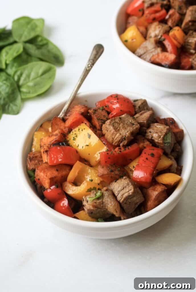 A bowl of freshly cooked Whole30 garlic steak bites with sweet potatoes and peppers, garnished and ready to eat.