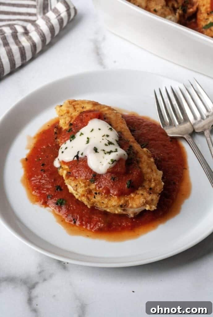 A white plate with a serving of Whole30 chicken parmesan, showing the crispy coating and creamy sauce.