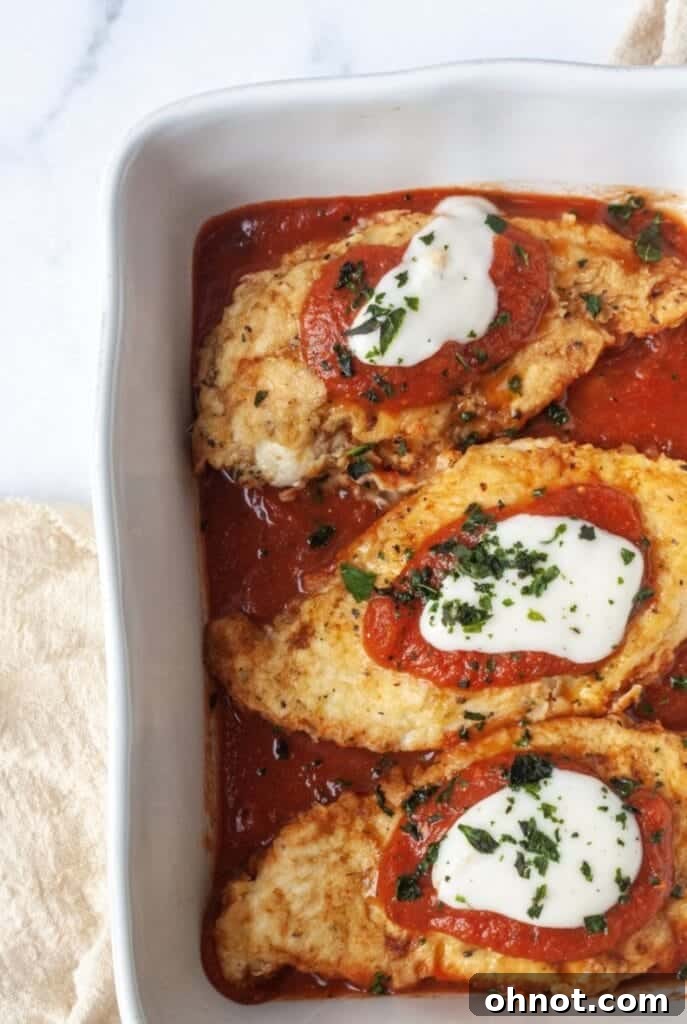 Whole30 Chicken parmesan presented attractively in a white casserole dish, garnished with fresh herbs.