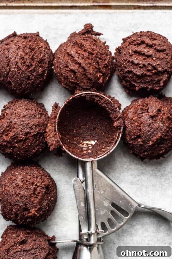 Close-up of scoops of brownie cookie dough on parchment paper, adorned with a sprinkle of sea salt before baking.