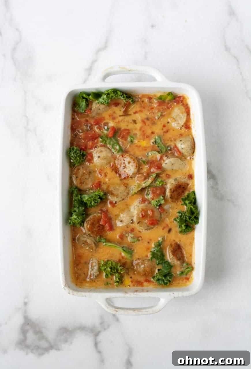 Close-up of layers: partially baked sweet potato, kale, and then cooked sausage and onions in a casserole dish