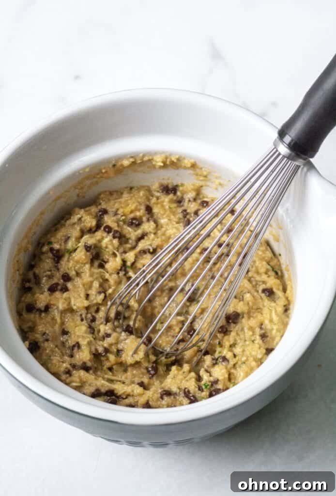 Zucchini muffin batter in a mixing bowl with mini chocolate chips folded in, ready for baking.
