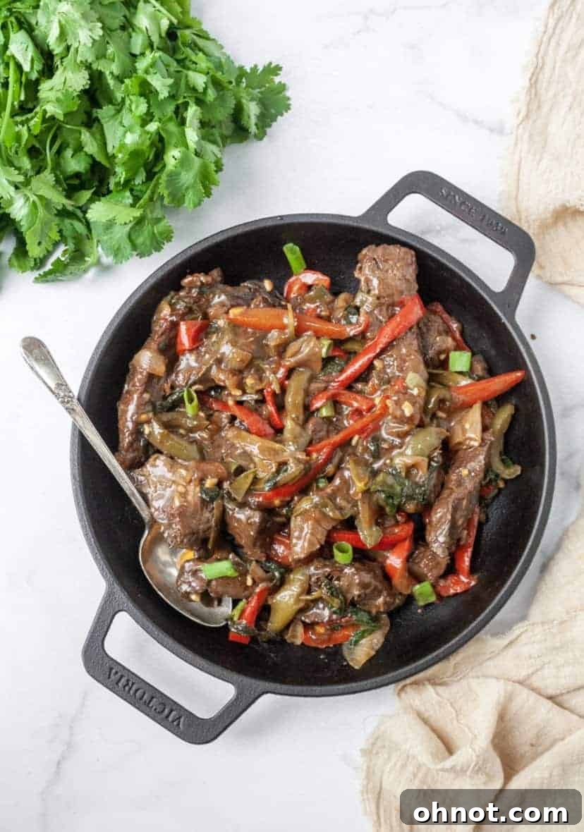 Whole30 Thai Basil Steak with vibrant bell peppers and fresh green onions simmering in a large skillet on the stovetop.