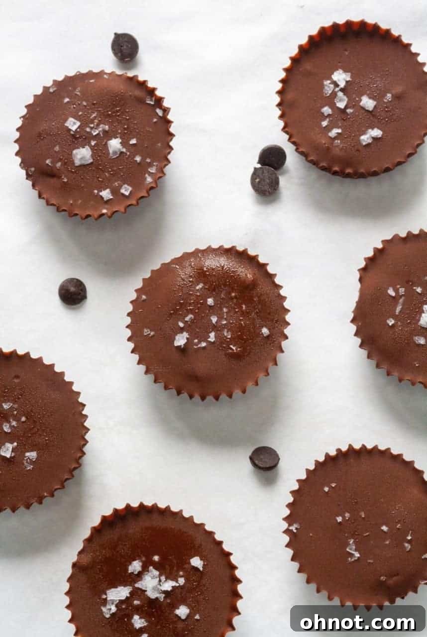A muffin tray filled with partially assembled pumpkin chocolate cups, showing the creamy orange pumpkin filling topped with a fresh layer of dark chocolate and a delicate sprinkle of flaky sea salt. This stage captures the cups just before their final freeze.
