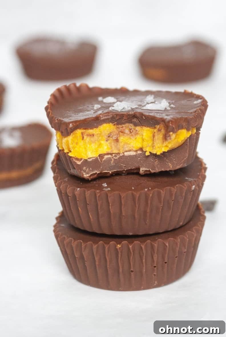 A close-up shot of a single pumpkin chocolate cup, cut in half to show the distinct layers of chocolate and pumpkin filling, with a focus on its creamy texture and the rich dark chocolate. This image highlights the cross-section of the dessert.