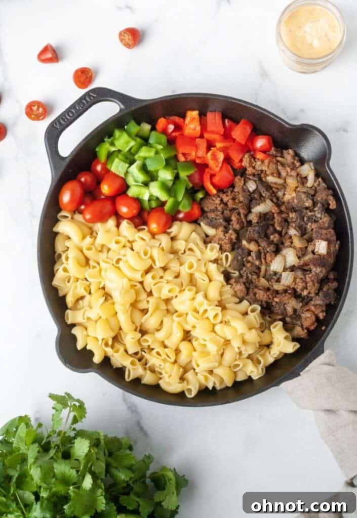 Ground beef, diced onion, and a blend of vibrant spices cooking in a cast iron skillet for the taco pasta salad base