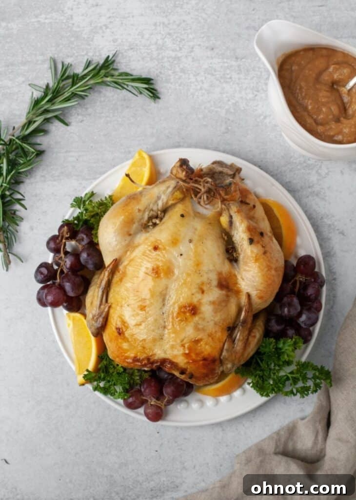 A beautifully roasted whole chicken, glistening and golden brown, surrounded by herbs.