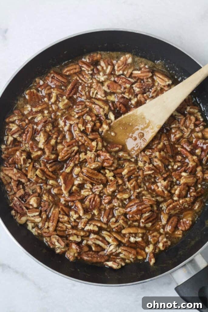 Paleo pecan pie filling being stirred in a black skillet on the stovetop, showing its rich, thick consistency.