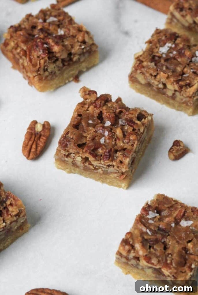 Freshly baked Paleo pecan pie bars cooling on a white backdrop, ready to be sliced and enjoyed.