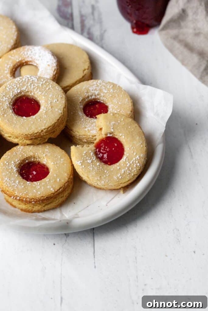 A stack of beautifully assembled Gluten Free Linzer cookies with raspberry jam on a white plate, ready to be enjoyed.
