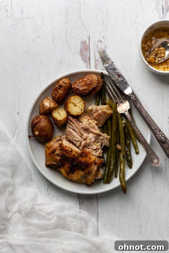 A white plate showcasing a serving of perfectly roasted sheet pan chicken thigh, surrounded by golden fingerling potatoes and tender green beans, ready to enjoy.