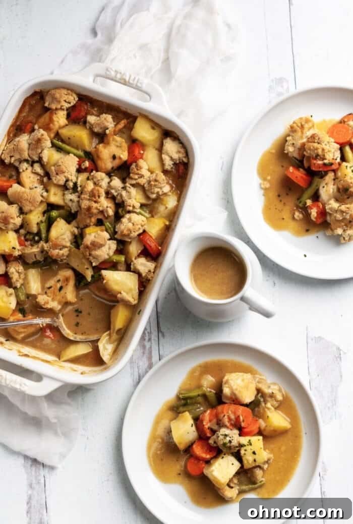 A beautifully presented Whole30 chicken pot pie casserole on a white backdrop, garnished with fresh herbs and a side of Whole30 gravy.